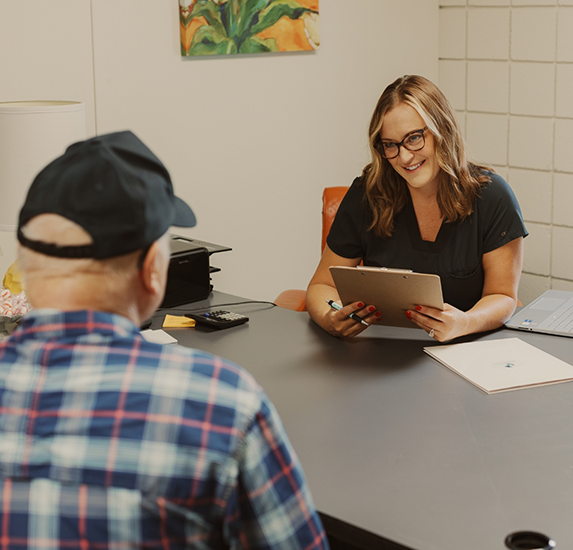 Laura sitting across a table from a patient while holding a clipboard