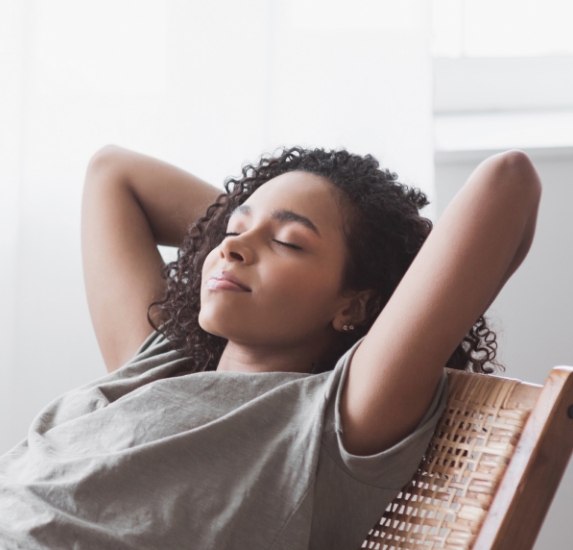 Young woman leaning back in a chair with eyes closed and her hands behind her head